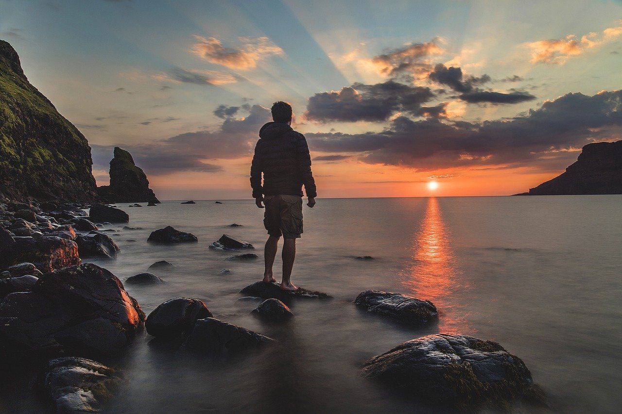 Man standing on a beach at sunset, gazing at the horizon, symbolizing independence and inner peace.